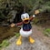 Donald Duck wearing a lumberjack outfit in a wide arm pose next to a creek in Alaska